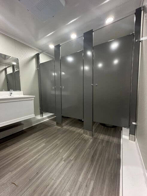 Close-up interior view of a toilet stalls inside a portable restroom trailer, featuring a porcelain toilet, a trash receptacle, and wainscoting on the wall.